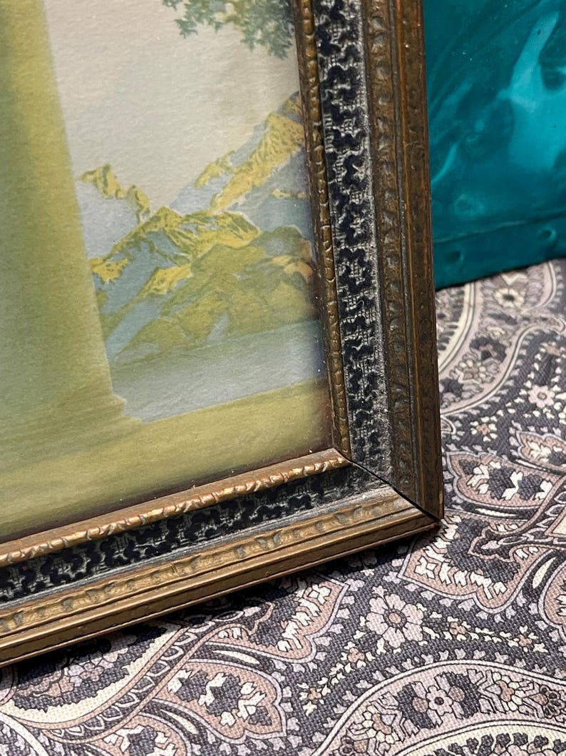 May include: A framed picture with a landscape scene of mountains and water. The frame is gold with a black inner border.