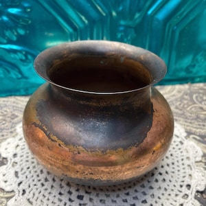 May include: A copper vase with a rounded body and a wide, flared opening. The vase has a rustic, aged appearance with a dark patina.