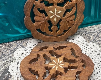 May include: Two intricately carved wooden coasters with a floral design. Each coaster features a white inlay in the center.