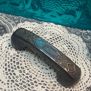 May include: A black vintage rotary phone handset with intricate floral designs etched into the surface.