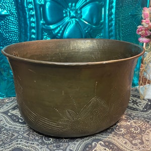 May include: A large, round, hammered copper planter with an intricate floral design. The planter is brown and has a shiny finish.