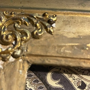 K&ouml;nnte beinhalten: Nahaufnahme eines verzierten goldfarbenen Rahmens mit einem dekorativen Design. Der Rahmen ist aus Holz und hat eine patinierte Oberfl&auml;che.
