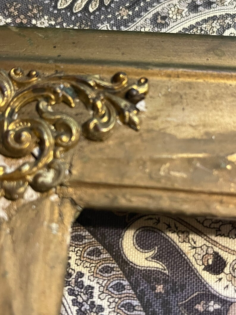 K&ouml;nnte beinhalten: Nahaufnahme eines verzierten goldfarbenen Rahmens mit einem dekorativen Design. Der Rahmen ist aus Holz und hat eine patinierte Oberfl&auml;che.