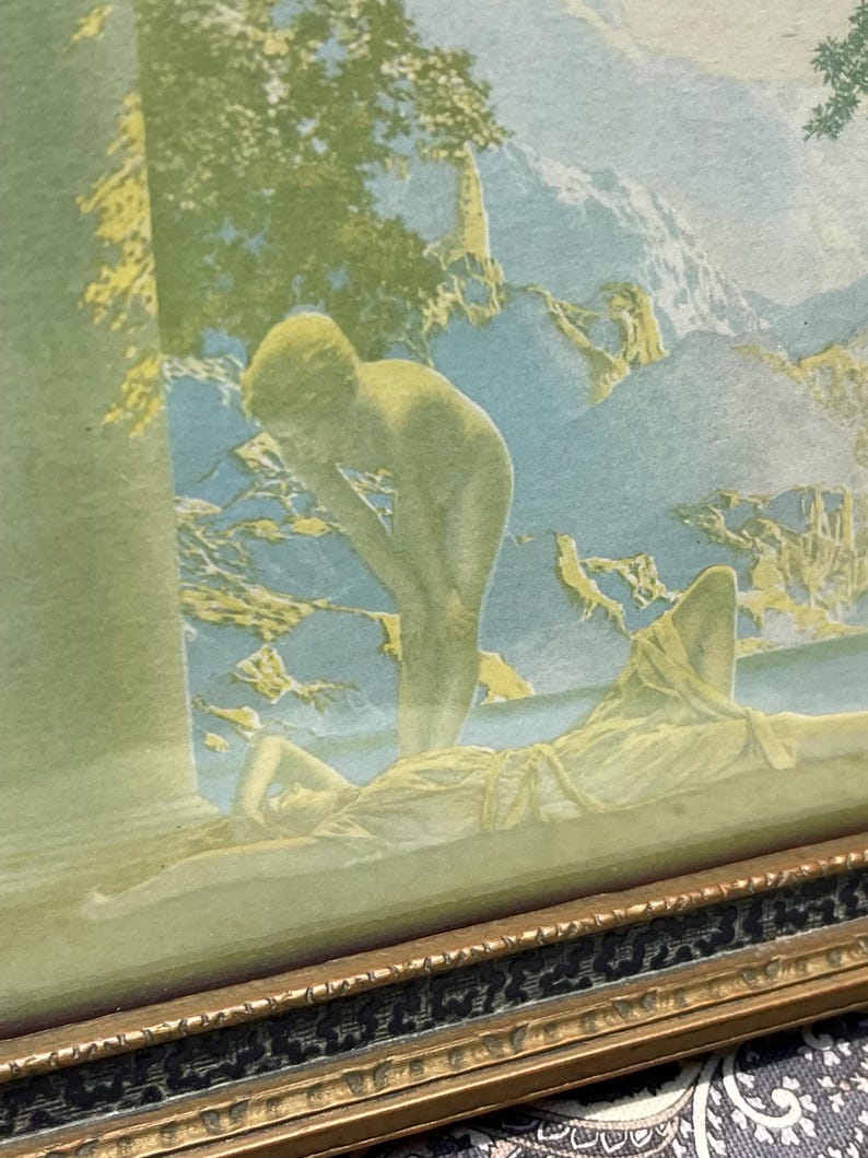 May include: A vintage framed print of a painting depicting two nude figures in a landscape setting. The figures are in a soft, muted color palette of green, blue, and yellow. The print is framed in a gold-colored frame with a black and gold patterned border.