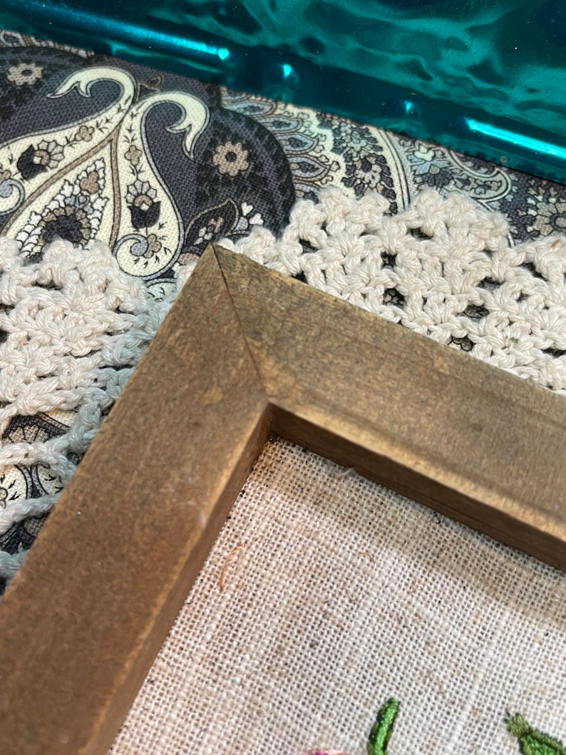 May include: Close-up of the corner of a brown wooden frame surrounding a piece of beige linen fabric. The frame is made of wood with a dark brown stain.