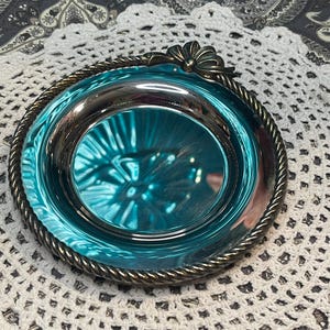 May include: A silver-plated trinket dish with a rope-like rim and a decorative bow-shaped handle. The dish has a teal blue interior.