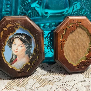 May include: Two octagonal wooden picture frames with ornate carvings. One frame has a portrait of a woman with a pearl tiara and the other frame is empty.