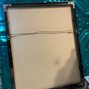 May include: A black picture frame with a white mat and a black wire hanging system. The frame is on a patterned surface.