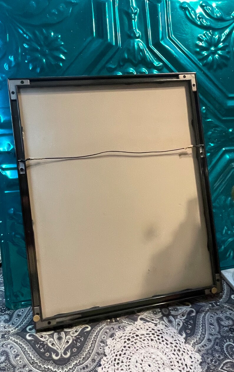 May include: A black picture frame with a white mat and a black wire hanging system. The frame is on a patterned surface.
