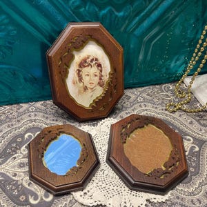 May include: Three vintage wooden picture frames with an octagonal shape. One frame contains a portrait of a child, another has a mirror, and the third has a tan backing. The frames have a dark brown finish and decorative cut-out edges.