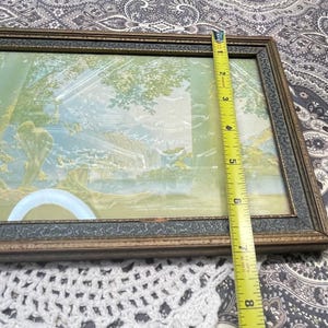 May include: A vintage framed picture with a light blue and green landscape scene. The frame is made of wood with a dark brown finish and a decorative gold trim.