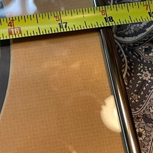 May include: A close-up of a yellow measuring tape with black markings. The tape is measuring the width of a brown wooden frame. The numbers 16, 17, 18 are visible on the tape.