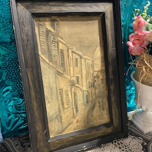 May include: A framed black and white drawing of a street scene with buildings and a person walking in the distance. The frame is black with a distressed finish.
