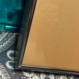 May include: Close-up of the corner of a gold-colored picture frame with a black border.