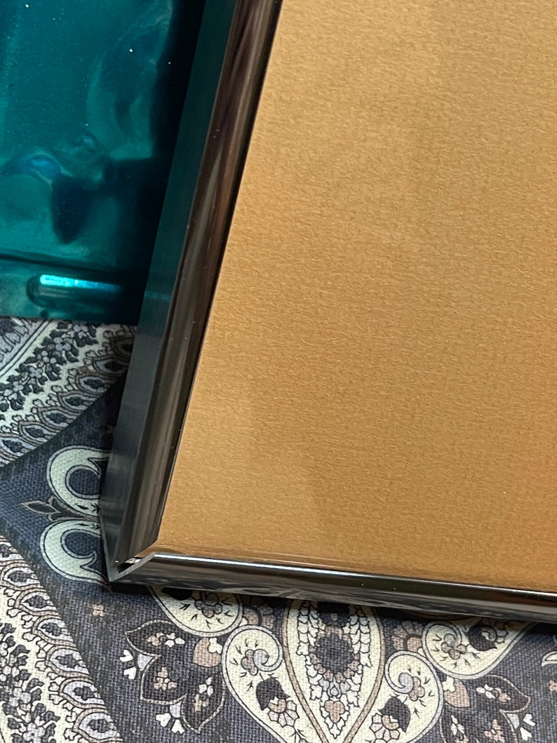 May include: Close-up of the corner of a gold-colored picture frame with a black border.