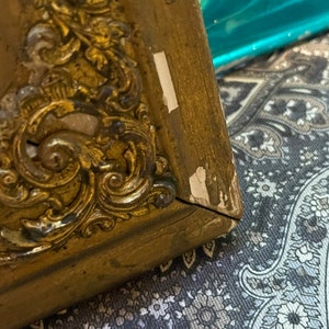 K&ouml;nnte beinhalten: Ein goldfarbener Bilderrahmen mit verzierten Details. Der Rahmen ist an der rechten unteren Ecke leicht besch&auml;digt.