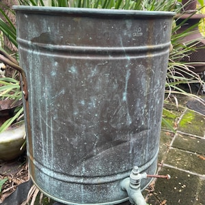 May include: A vintage copper water cooler with a spigot. The cooler is 10 gallons and has a green patina. It is sitting on a decorative base.