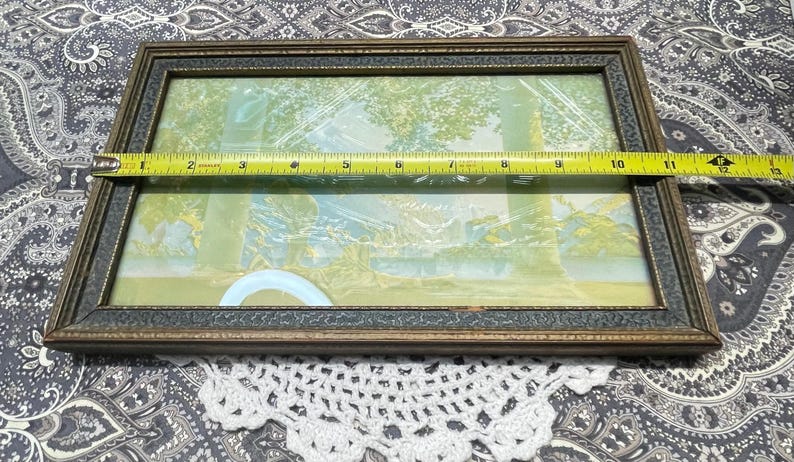 May include: A vintage framed print with a light blue and green landscape scene. The frame is made of wood with a dark brown finish and a gold trim.
