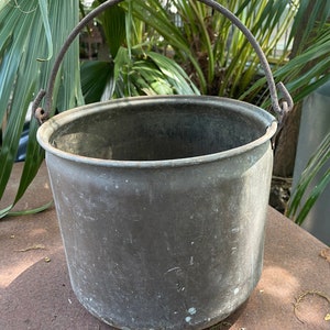 May include: A vintage copper bucket with a rusty metal handle. The bucket is weathered and has a patina finish.