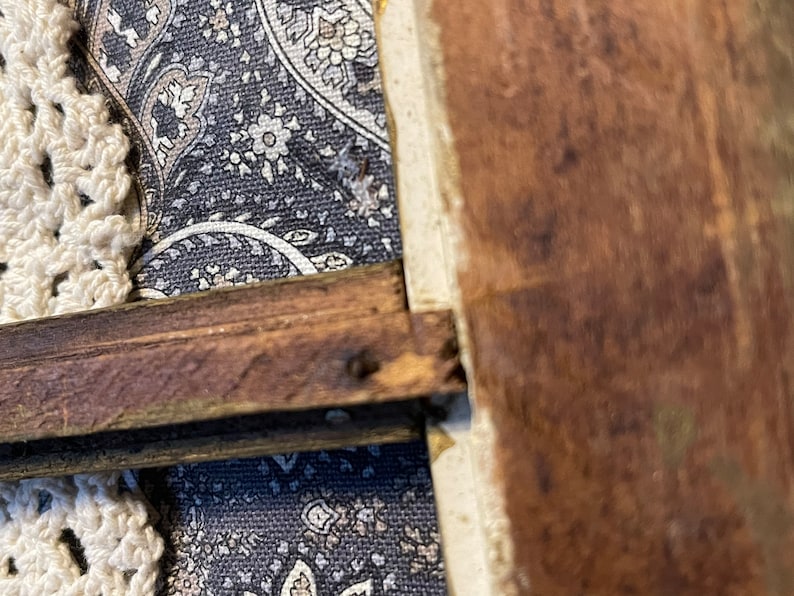 K&ouml;nnte beinhalten: Nahaufnahme eines Holzrahmens mit dunkelbrauner Oberfl&auml;che. Der Rahmen ist an einem Stoffhintergrund mit Paisley-Muster befestigt.