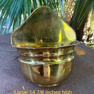 May include: A large, vintage brass planter with a distinctive shape. The planter is approximately 14 7/8 inches high and features a triangular top section above a rounded bowl. The brass has a warm, golden hue and shows signs of age.