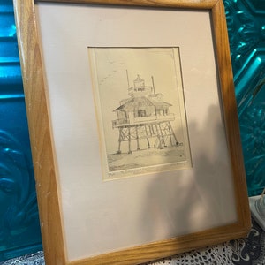 May include: A framed black and white drawing of a lighthouse on stilts. The drawing is titled "The Diamond Shoals Light House,  Salvo, North Carolina".