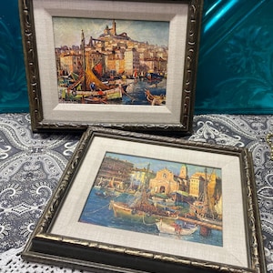 May include: Two framed oil paintings depicting harbor scenes with boats, buildings, and hills. Each painting is housed in a dark, ornate, textured frame with a wide, light-colored fabric matting. The artist signature Colombini is visible.