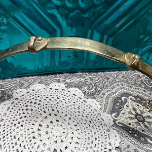 May include: A curved, brass-toned metal towel rack with heart-shaped accents. The rack has two curved hooks on each end and is displayed on a patterned surface with a white doily.