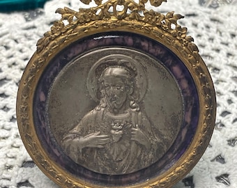 Medallón antiguo o vintage pequeño con marco de metal ornamentado del Sagrado Corazón de Jesús con borde que imita piedra, soporte de caballete y colgador.