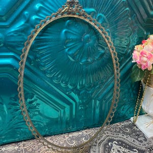 May include: A gold-toned oval-shaped frame with a decorative cherub design at the top. The frame is ornate and has a delicate, intricate design.