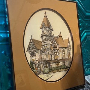 May include: A framed print of a detailed drawing of a large, ornate Victorian house with a tower. The house is painted in shades of brown, gray, and white. The print is set against a brown background and has a white oval border. The text "Leland Stanford Mansion, Garden Manor, Loomis, California" is printed at the bottom of the print.