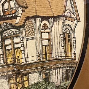 May include: A vintage illustration of a Victorian-style house with a brown roof, white walls, and intricate details. The house has multiple windows, a balcony, and a porch. The illustration is framed in a brown oval frame.