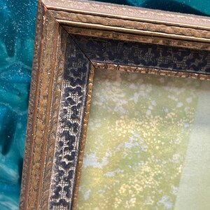 May include: A gold picture frame with a black and gold patterned border. The frame is empty and has a light green background.