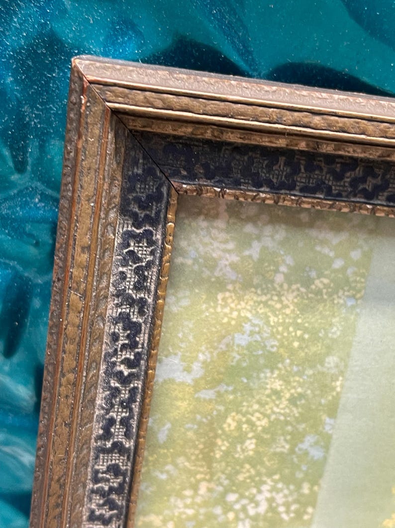 May include: A gold picture frame with a black and gold patterned border. The frame is empty and has a light green background.