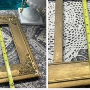 K&ouml;nnte beinhalten: Ein goldfarbener Bilderrahmen mit verzierten Details, der zwei wei&szlig;e H&auml;keldeckchen h&auml;lt. Der Rahmen befindet sich auf einer gemusterten Stoffoberfl&auml;che.