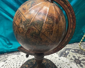 May include: A vintage-style globe featuring a sepia-toned map with visible longitudinal lines. The globe is mounted on a dark wooden stand with a circular base decorated with zodiac symbols and a curved meridian arc labeled with Italian text.
