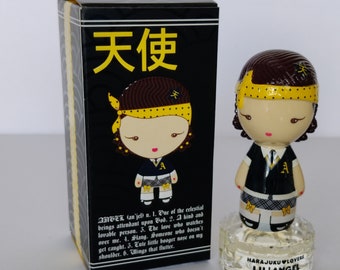 May include: A small, clear glass bottle with a black and white doll figurine on top. The doll has brown hair, a yellow headband, and a black and white plaid skirt. The bottle has a label that says "Harajuku Lovers Lil' Angel".