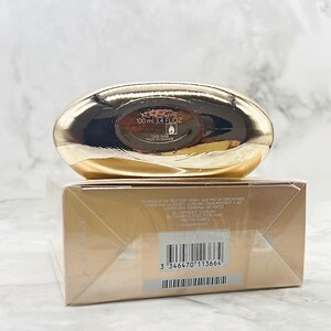 K&ouml;nnte beinhalten: Eine goldfarbene Parf&uuml;mflasche und -schachtel. Die Flasche ist oval und tr&auml;gt den Text "EAU DE TOILETTE 100 ml 3.4 FL OZ". Die Schachtel hat Text und einen Barcode.