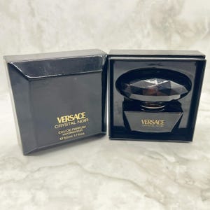 May include: A black Versace Crystal Noir Eau de Parfum bottle and box set. The bottle is a dark, faceted design, and the box features gold lettering. The set includes a 50ml, 1.7 fl oz bottle.