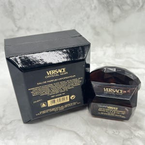 May include: A black box and a dark brown perfume bottle with the text "VERSACE CRYSTAL NOIR". The bottle is 1.7 fl. oz. and has a faceted design. The box contains the ingredients and other details.