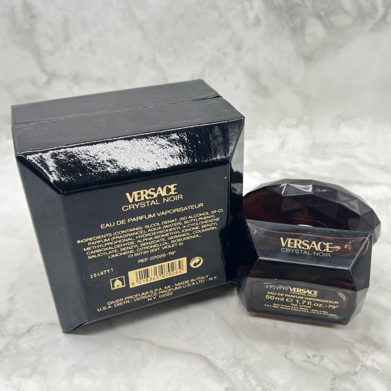 May include: A black box and a dark brown perfume bottle with the text "VERSACE CRYSTAL NOIR". The bottle is 1.7 fl. oz. and has a faceted design. The box contains the ingredients and other details.