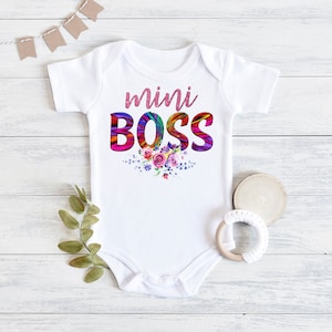 May include: White baby onesie with the text "mini BOSS" in rainbow colors with a floral design underneath.