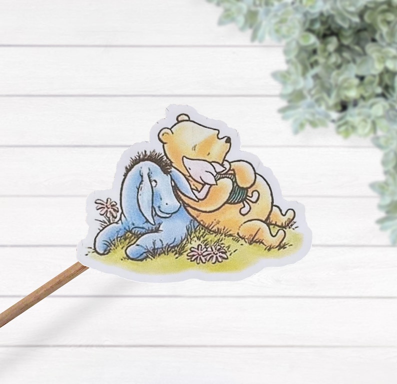 May include: A sticker featuring Winnie the Pooh and Piglet. Winnie the Pooh is a yellow bear with a red shirt and Piglet is a pink pig. They are both smiling and hugging each other. The sticker is set against a white background with green grass and pink flowers.