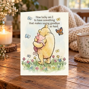May include: A greeting card featuring a watercolor illustration of Winnie the Pooh hugging Piglet in a field of flowers with butterflies. The text reads: How lucky am I to have something that makes saying goodbye so hard.