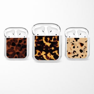 Może przedstawiać: Trzy przezroczyste plastikowe etui z różnymi wzorami w stylu żółwia dla AirPods.