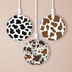 Puede incluir: Tres cargadores inalámbricos con diferentes diseños de estampado de vaca. Las almohadillas son blancas con manchas negras, marrones y tostadas.