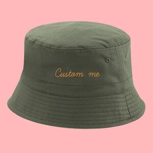 Peut inclure: Un chapeau bob vert avec le texte "Custom me" brodé en fil orange.