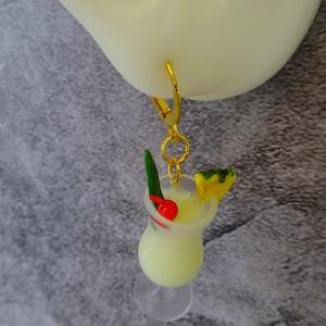 May include: Gold hoop earring with a miniature glass of a tropical drink with a pineapple wedge, a green sprig, and a red cherry.