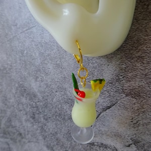 May include: Gold hoop earrings with a dangling charm of a miniature glass of a tropical drink with a pineapple wedge, a green garnish, and a red cherry.