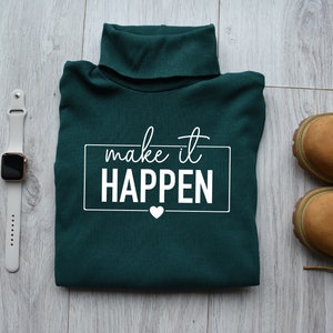 May include: A dark green turtleneck sweater with the text "make it HAPPEN" in white lettering. A small white heart is below the text.